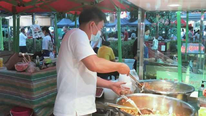 Vu Hồng Đào đang phục vụ món chân gà nướng cho khách tại chợ Urumqi, tháng 8/2021. Ảnh: Thenews