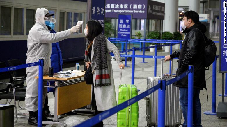 Một nhân viên an ninh kiểm tra nhiệt độ của hành khách đến sân bay quốc tế Phố Đông Thượng Hải.