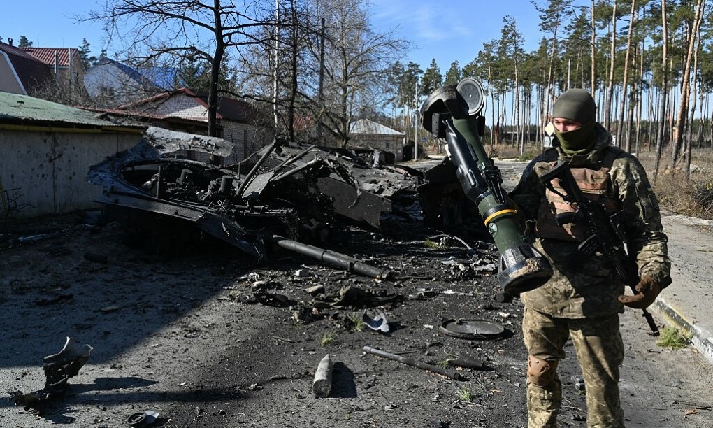 Binh sĩ Ukraine bên cạnh xác xe tăng Nga bị thiêu rụi (Ảnh: AFP)